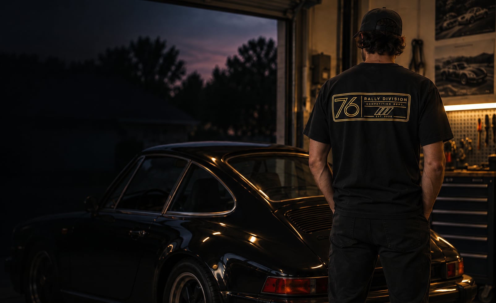 An enthusiast in a 76 Rally Division tee beside a classic coupe in the garage